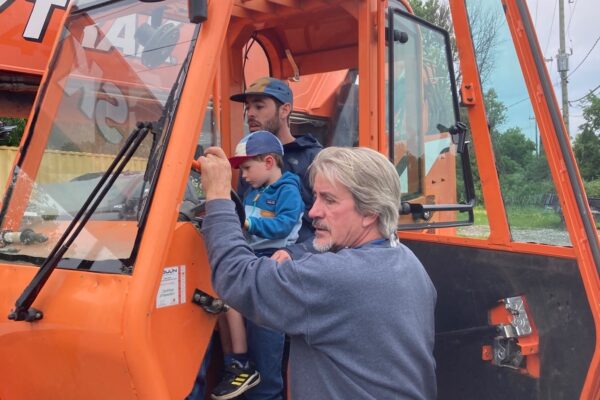 Three people in an orange tractor, outdoors.