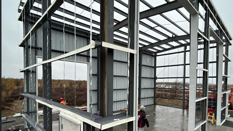 Steel building under construction site with workers present.